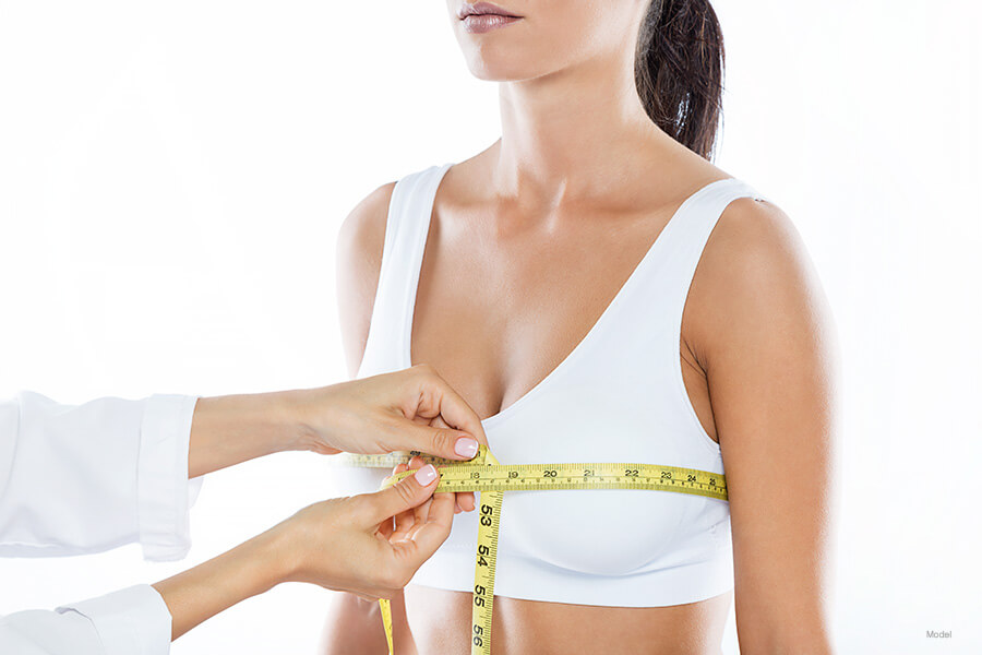 A woman in a white bra getting her breasts measured by a doctor