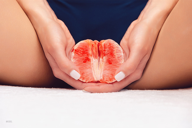 closeup of a model holding a grapefruit with between her legs with two hands.